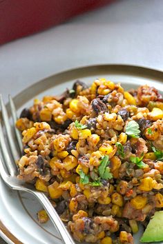 a white plate topped with corn salad next to an avocado