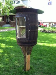 a wooden barrel shaped mailbox sitting on top of a lush green field next to a house