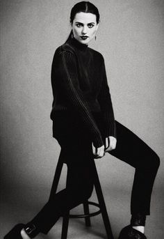 a black and white photo of a woman sitting on a stool