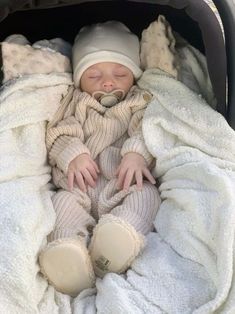 a baby is sleeping in a stroller with white blankets on it's sides