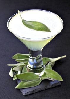 a green drink garnished with leaves on a black table