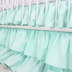 a baby crib with green ruffles and white rails