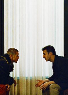 two men are talking in front of a window