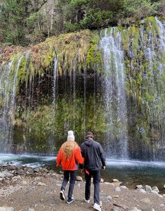 two people standing in front of a waterfall with water cascading down the side