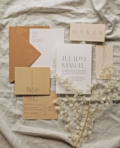 the wedding stationery is laid out on top of the bed sheet, with white flowers and brown envelopes