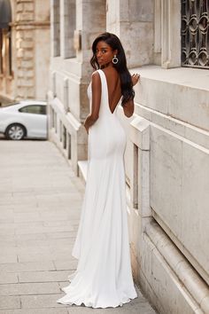 a woman in a long white dress leaning against a wall with her back to the camera