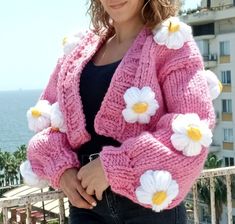 a woman wearing a pink cardigan with white flowers on the front and yellow centers