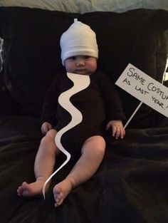 a baby sitting on top of a bed holding a sign that says same costume as last year