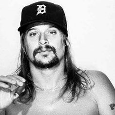 a shirtless man with long hair and a baseball cap holding something in his hand