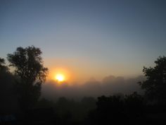 the sun is setting behind some trees in the foggy morning sky with low clouds