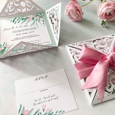 the wedding stationery is decorated with pink flowers and greenery, along with an origami style bow