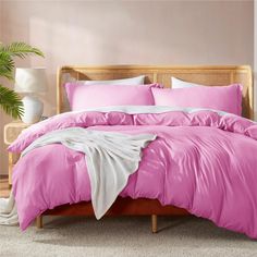 a bed with purple comforter and pillows in a pink room next to a potted plant