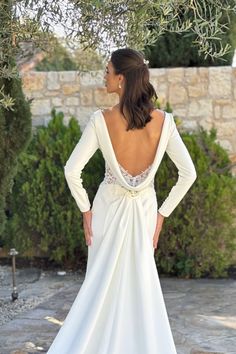 a woman in a white wedding dress is looking back at the camera while standing under an olive tree