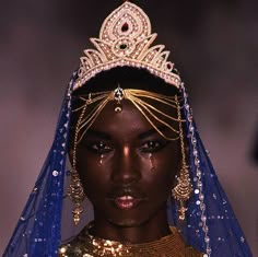 a model wears an elaborate head piece with gold and blue veils on her head