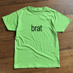 a green t - shirt with the word brat on it sitting on a wooden floor