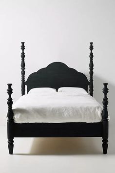 a black bed frame with white sheets and pillows on the headboard, in front of a white wall