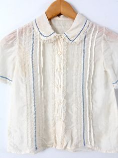 "This is a vintage silk blouse circa 1920s. The cream silk top features pin tuck pleats down the front with blue laced stitching and lace trim. It buttons closed. CONDITION In great condition. Approximate Fit: XS MEASUREMENTS Bust: 30\" ... 76.2 cm Length: 18\" ... 45.7 cm Shoulders: 12\" .. 30.5 cm Outside Sleeve: 8\" ... 20.3 cm HOW WE MEASURE * Blouse measured lying flat * Bust measured armpit to armpit * Length measured down the center of the back * Shoulders measured between the shoulder se Cheap Vintage Cream Tops, Silk Tops With Lace Trim For Daywear, Vintage Silk Short Sleeve Blouse, Vintage Lace Collar Button-up Top, Vintage Silk Blouse With Short Sleeves, Vintage Silk Collared Top, Daywear Button-up Blouse With Pintucks, Button-up Daywear Blouse With Pintucks, Button-up Blouse With Pintucks For Daywear