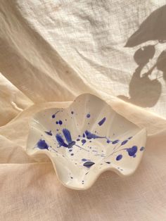 a white and blue bowl sitting on top of a cloth covered table next to a shadow of an umbrella