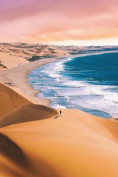 a person walking on top of a sand dune next to the ocean with waves coming in