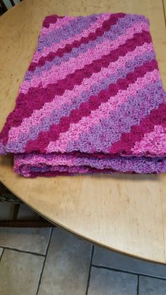 a pink and purple crocheted blanket sitting on top of a wooden table next to a chair