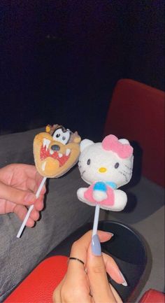 two hello kitty lollipops are being held by someone's hand while sitting in a chair