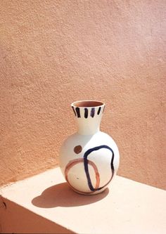 a small white vase sitting on top of a table next to a wall and window