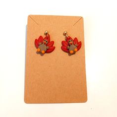 a pair of red and orange bird earrings sitting on top of a piece of cardboard