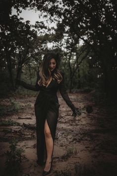 a woman in a black dress is walking through the woods with her legs spread out