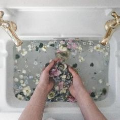 a person washing their hands in a bathtub with flowers on the floor and gold faucets