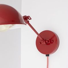 a red lamp is on the wall next to a white wall with a black cord