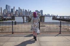 a woman with pink hair is standing near a fence and looking at the city skyline