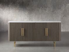 a sideboard with two gold handles on the front and sides, against a concrete wall