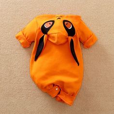 an orange baby romper laying on the floor with eyes painted on it's face