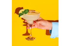 a hand holding a drink with a lime on the rim, against a yellow background