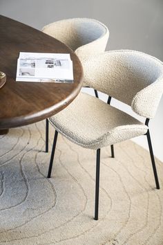 two chairs sitting on top of a rug next to a wooden table with a magazine