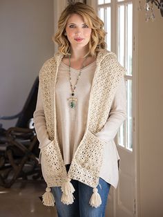 a woman standing in front of a door wearing a white sweater and tasselled cardigan