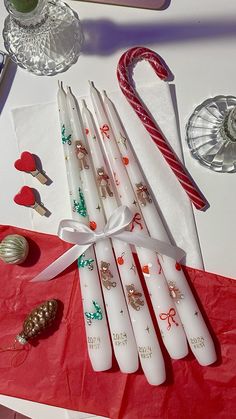 a table topped with white candles and candy canes next to other items on top of a red cloth