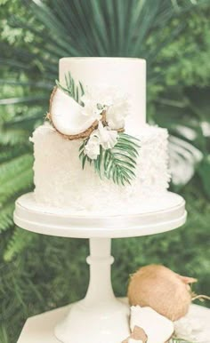 a white wedding cake with flowers and coconuts on the top is surrounded by greenery