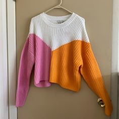 an orange, pink and white sweater hanging on a door