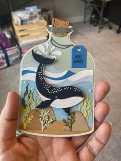 a hand holding up a bottle shaped like a whale with the words make waves on it