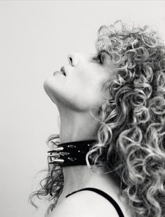 a woman with curly hair wearing a black leather choker and looking up into the sky