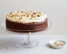 a cake with white frosting and walnuts on top sitting on a glass plate