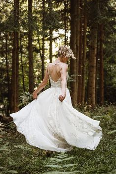 a woman in a white dress is walking through the woods with her back to the camera