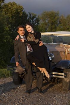 a man and woman posing in front of an old car