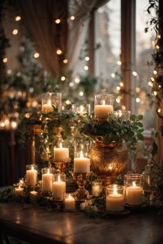 candles and greenery are arranged on a table in front of a window with lights