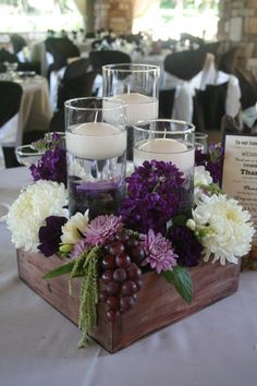 a wooden box filled with flowers and candles on top of a white tablecloth covered table