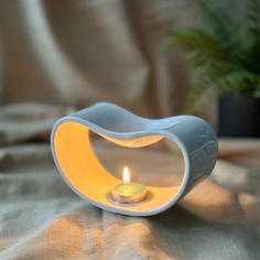 a small white candle holder with a yellow light in it's center on a bed