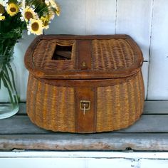 a wicker box sitting on top of a wooden bench next to flowers and vases