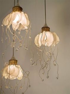 three lights hanging from the ceiling with white flowers on them and vines attached to them