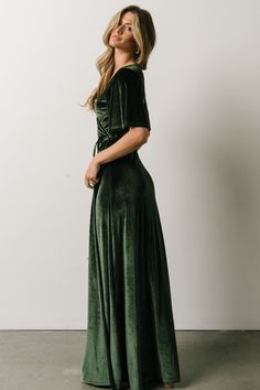 a woman in a green velvet dress standing up against a white wall and looking off to the side